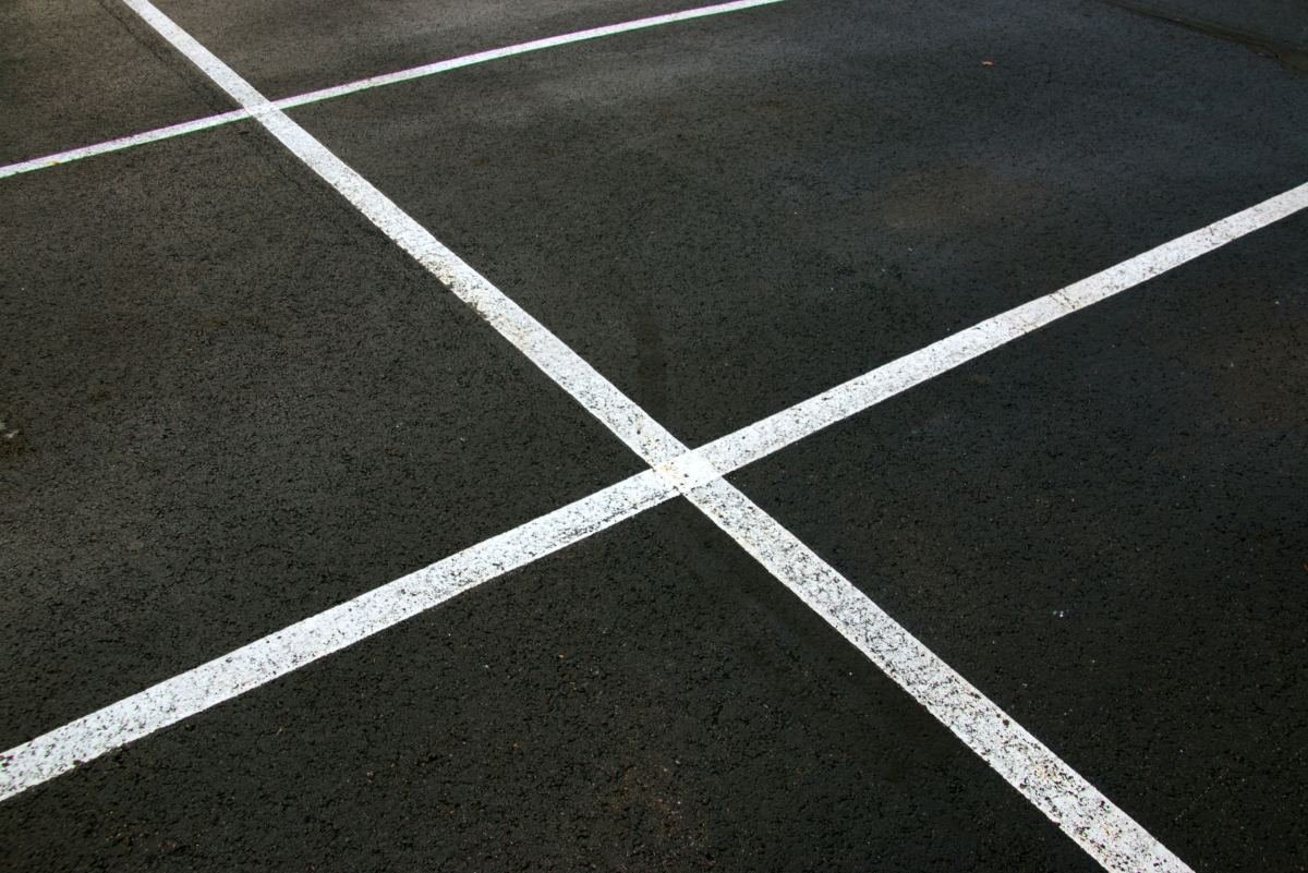 Weathered commercial asphalt parking lot surface with cracking and faded striping in need of repair